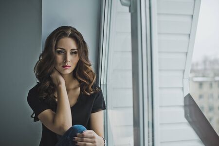 Beautiful slender girl sitting on the windowsill.