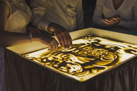 The process of drawing a picture of the sand on the illuminated glass.