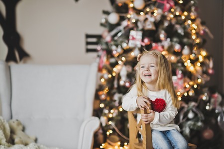 A little girl with a red heart on the clothes sitting in front of the tree.の写真素材