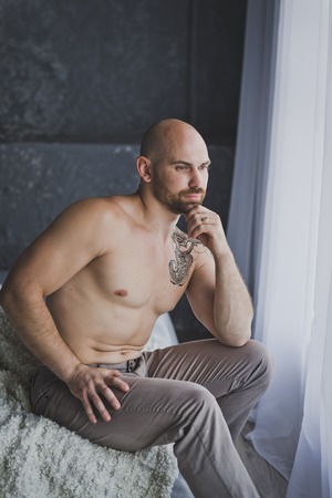 Bald brutal man sits pensively at the window.の写真素材