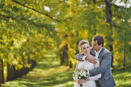 The bride and groom embrace and walk through shady spruce Avenue.の写真素材