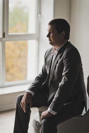 The groom in a business suit sitting at a huge lit window.の写真素材