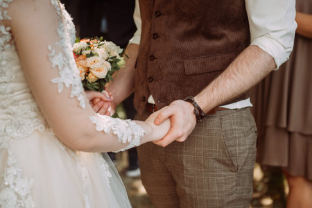 Gentle embrace of the hands of the newlyweds with wedding rings.