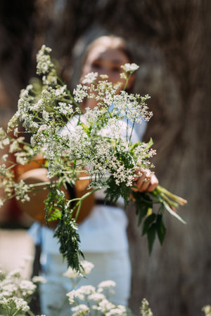 A walk of a joyful girl with a bouquet of daisies in a summer park.