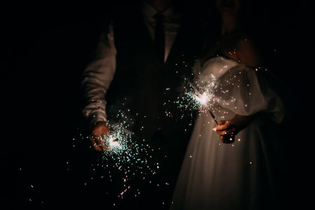 Night photo of hands holding sparklers in the dark.