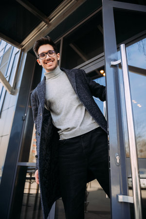 He is wearing glasses and is standing in front of a door.