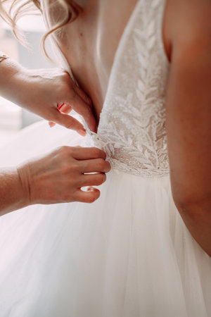 The dress is ivory with embellishments and lace, and the person is likely a bride preparing for a wedding ceremony. The setting is indoors, possibly in a bridal shop or dressing room.の写真素材