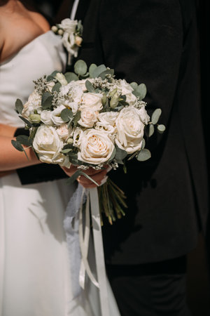 The woman is wearing a wedding dress, and both individuals are holding a bouquet of roses.の写真素材
