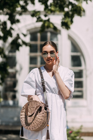 They are wearing sunglasses, holding a handbag, and smiling. The background includes a building and street fashion elements.の写真素材