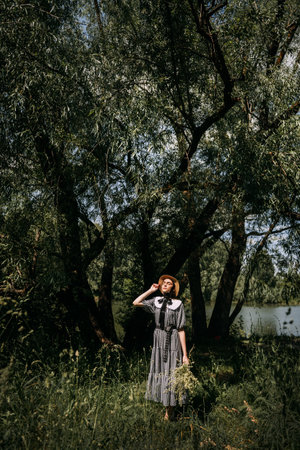 The person is wearing a dress and is surrounded by grass and plants. It depicts a woman enjoying the summer weather.の写真素材