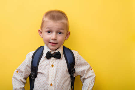back to school. A blond funny boy with a backpack in a light shirt on a yellow background looks at the camera. ?opy space. education.の写真素材