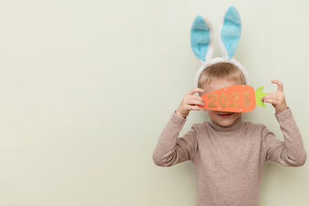 A funny boy in the guise of a rabbit holds a carrot with the numbers of the New Year 2023 on a light background with a space to copy. The concept of the New Yearの写真素材