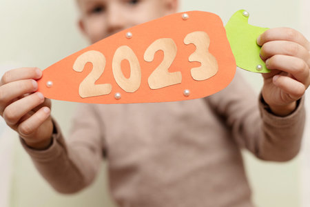 A funny boy in the guise of a rabbit holds a carrot with the figures of the New Year 2023 close-up. The concept of the New Yearの写真素材