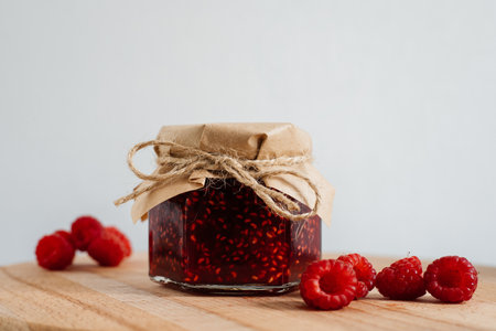 Delicious homemade raspberry jam presented in charming jar on a rustic wooden board, adorned with paper and twine. Fresh raspberries add a pop of color. Perfect for banners, menus, or recipe illustrationsの写真素材