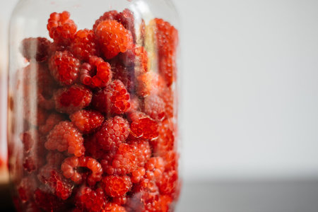Close-up of raspberries in a glass jar on a white background