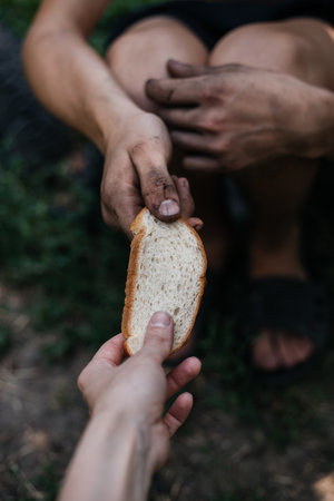 Helping the homeless poor. Moment of kindness: offering bread to a homeless person. Conveys compassion and humanity in adversity. Ideal for themes of charity and empathyの写真素材