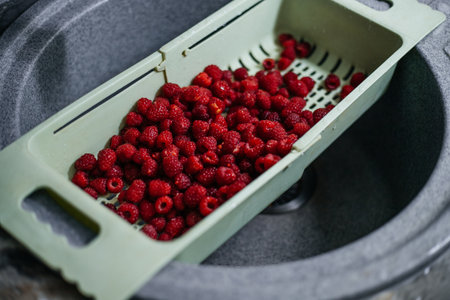Preparation of raspberries for making jam, compote. Washing in colander in the kitchen in the sink
