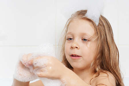 A cute, beautiful girl with long hair plays in the bathroom with soap bubbles. Children's emotions...