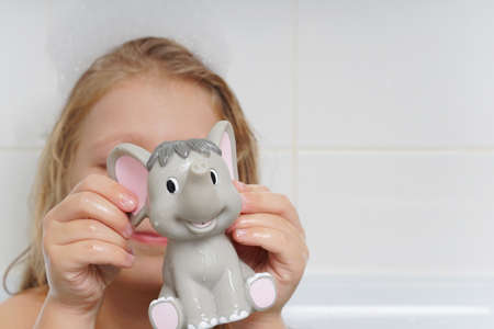 A cute, beautiful, cheerful little girl with long hair is playing in the bathroom with an elephant....