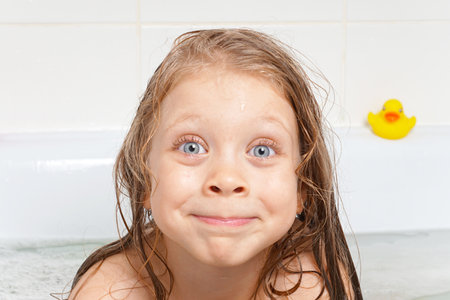 Cute, beautiful, cheerful little girl with long hair in the bathroom. Children's emotions with soap...