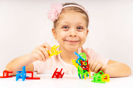 The girl is playing a board game. The child builds a tower of balancing chairs. Home education, learning, playing. The quarantined child is at home.の写真素材