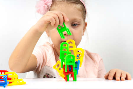 A tower of balancer chairs on a white table. The girl plays an educational board game at home self-isolation. The child plays with enthusiasmの写真素材