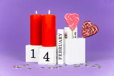 Valentines day purple trending background. 2 burning red candles, a perpetual calendar block with...