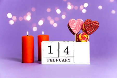 14 february purple trendy background with bokeh. 2 burning red candles, a perpetual calendar block with the date of February 14 and sweet as love caramel heartsの写真素材