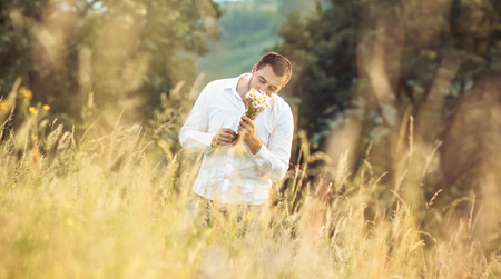 Man with flower standing in a grass - meadow. Leisure concept. Outdoor. Gorgeous guy smell camomileの写真素材