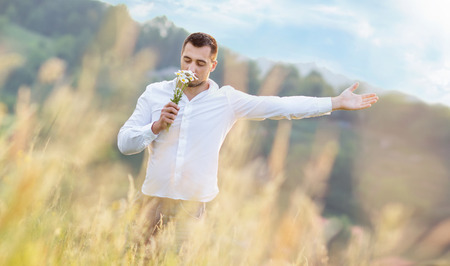Relaxed young man smell the flowers - camomile and showing freedom with his arm