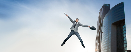 Businessman jumping in joy. Full length of smart happy man holding briefcase in the air. outdoorsの写真素材