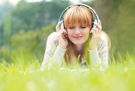 Beautiful young woman with headphones. Enjoy music outdoors. Girl repose or lie downの写真素材