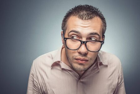 Young man looking furtively to side over dark gray background. Studio shotの写真素材
