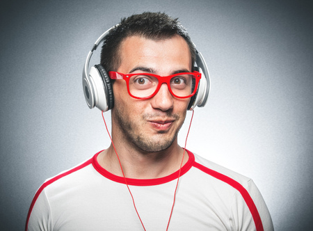 Portrait of a funny young man make a comic face and listening music with headphones against a dark gray backgroundの写真素材