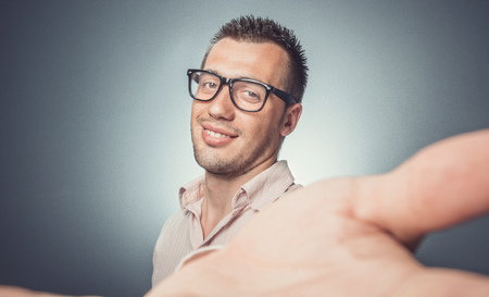 Selfie. Happy young man taking a selfie photo over dark gray background. Studio shotの写真素材