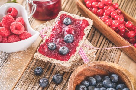 Pastry appetizers jam with blueberries and currant over toast serving on wooden table