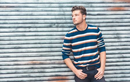 Fshionable young man posing  against wall in colored sweatshirt