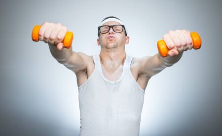 Funny weak man tries to lift a weight - dumbbells, isoalted on gray white.
Nerd male training - doing fitnessの写真素材