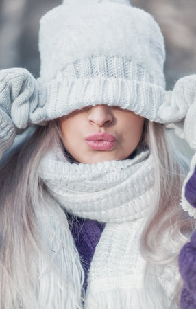 Winter portrait of young beautiful woman covering her face with woolen cap on winter day outdoors....