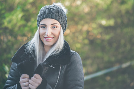 Smiling young woman in warm clothing on winter day outdoors. Happy girl wearing wool cap and black...