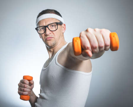 Funny weak man wit dumbbells doing exercising, isolated on gray white backgroundの写真素材