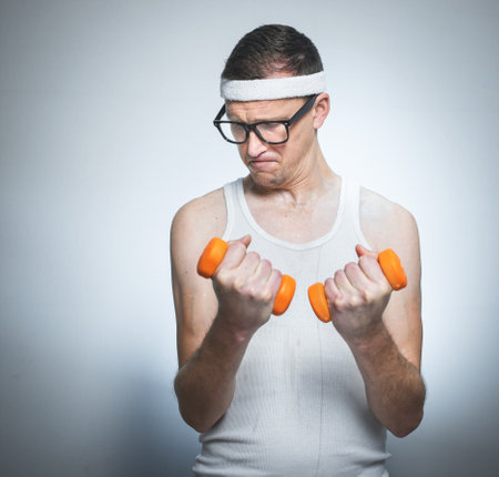 Funny weak man tries to lift a weight - dumbbells, isoalted on gray white. Nerd male training - doing fitnessの写真素材