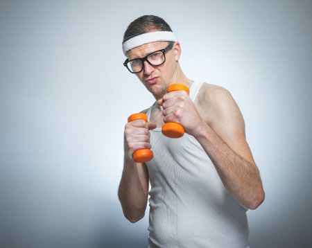 Funny weak man tries to lift a weight - dumbbells, isoalted on gray white. Nerd male training - doing fitnessの写真素材