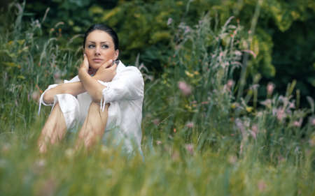 Beautiful woman sitting in a grass. Young girl relaxing on meadow, outdoors. Enjoy natureの写真素材