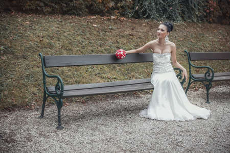 Young beautiful sitting on bench in park, outdoors. Marry woman. Wedding dayの写真素材