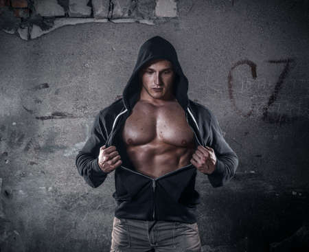 Epic muscular young man - fighter wearing hooded sweater and showing his breast muscle, frontal portrait of mystic bodybuilder, copyspace for textの写真素材