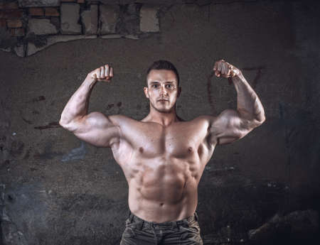 Bodybuilder showing hic biceps, young muscular man over grunge old wall, copyspace for textの写真素材