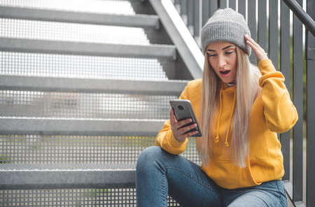 Astonished girl with smartphone. Trendy woman. Unbelievable message. Outdoor - outsideの写真素材
