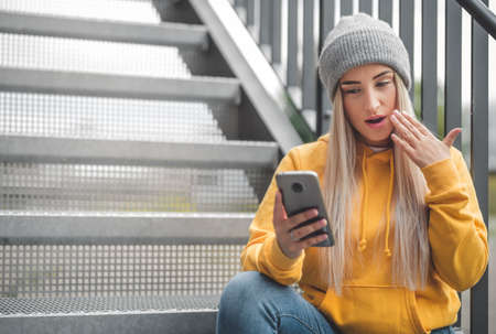 Astonished girl with smartphone. Trendy woman. Unbelievable message. Outdoor - outside
