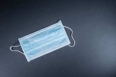 Medical face mask isolated on dark gray or black. Disposable surgical mask with rubber ear straps to cover the mouth and nose.の写真素材